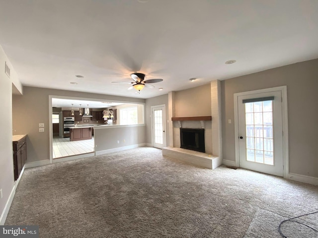 unfurnished living room featuring ceiling fan, a fireplace, baseboards, and light carpet