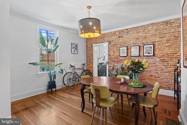 dining room with baseboards, brick wall, ornamental molding, and hardwood / wood-style flooring