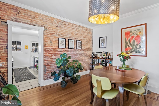 dining area featuring brick wall, baseboards, a chandelier, light wood-type flooring, and ornamental molding