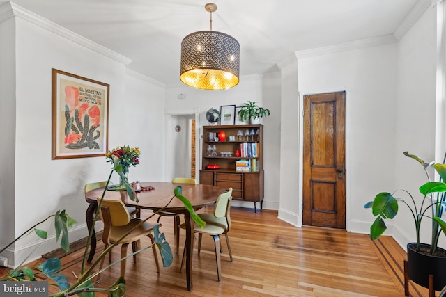 dining space featuring light wood finished floors, crown molding, and baseboards