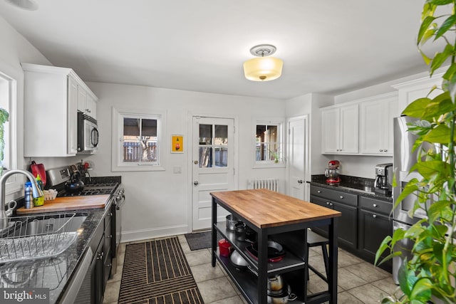 kitchen with a sink, stainless steel appliances, white cabinets, light tile patterned flooring, and wooden counters