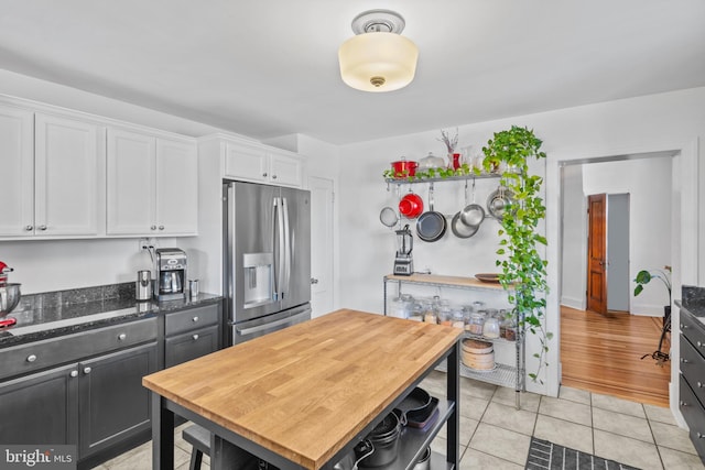 kitchen with dark stone countertops, light tile patterned floors, open shelves, white cabinets, and stainless steel fridge