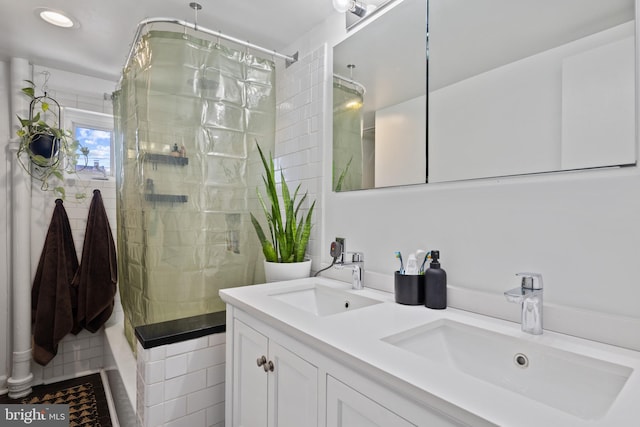 full bath with double vanity, tiled shower, and a sink