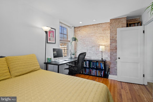 bedroom featuring baseboards, wood finished floors, and brick wall