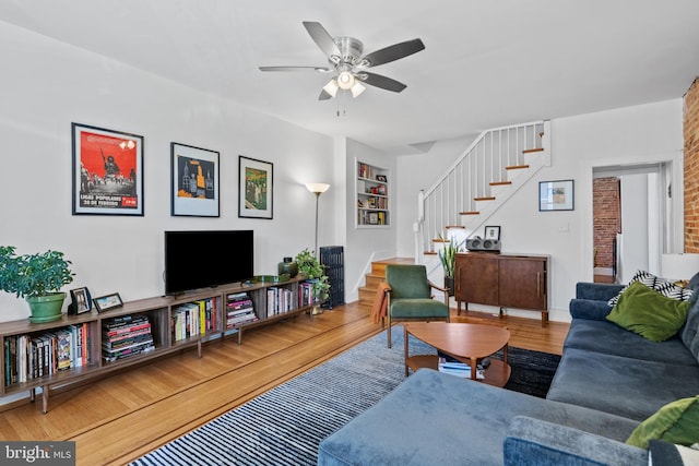 living room featuring a ceiling fan, stairway, and wood finished floors