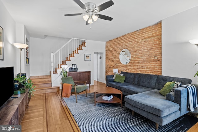 living area featuring stairs, hardwood / wood-style flooring, brick wall, and ceiling fan