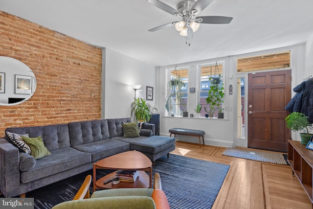 living area with brick wall, baseboards, a ceiling fan, and wood finished floors