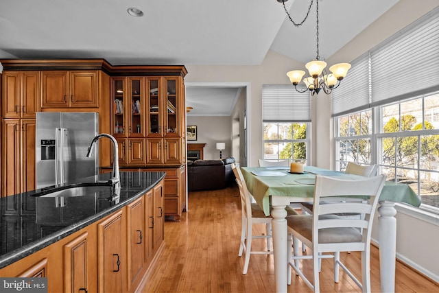 kitchen with dark stone countertops, brown cabinetry, light wood-style flooring, a sink, and high end refrigerator