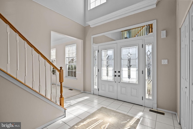 tiled foyer entrance with visible vents, crown molding, baseboards, stairs, and a towering ceiling