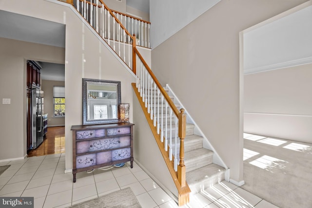 stairway featuring tile patterned floors, a high ceiling, and baseboards