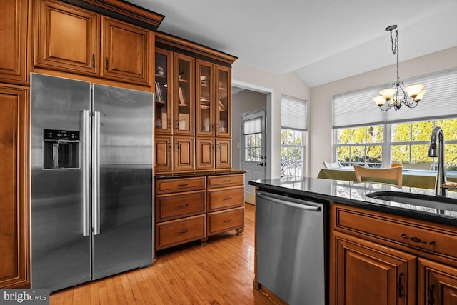 kitchen with brown cabinetry, lofted ceiling, a sink, hanging light fixtures, and appliances with stainless steel finishes