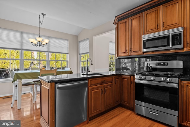 kitchen featuring light wood-type flooring, a sink, appliances with stainless steel finishes, a peninsula, and an inviting chandelier