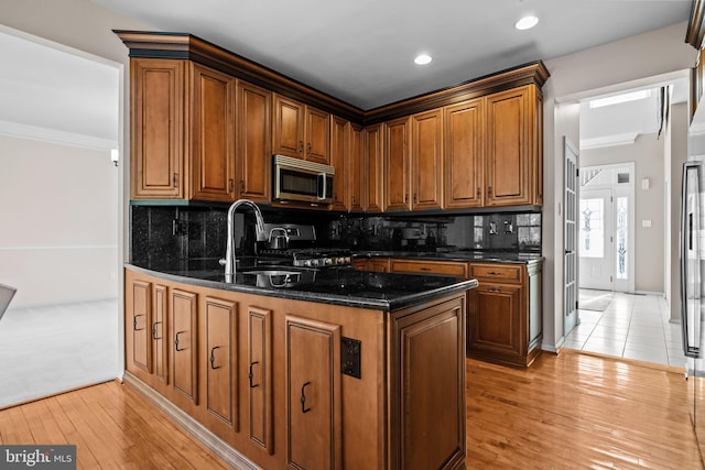 kitchen featuring gas stove, brown cabinets, light wood-style floors, stainless steel microwave, and tasteful backsplash