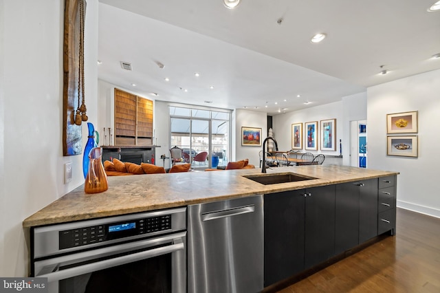 kitchen with dark wood-type flooring, open floor plan, appliances with stainless steel finishes, dark cabinetry, and a sink