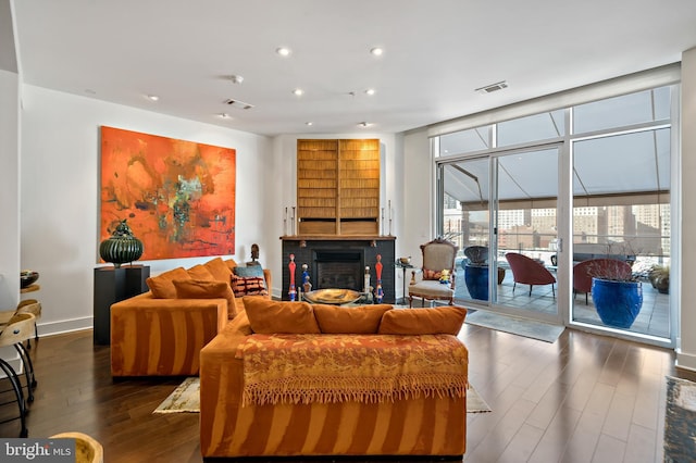 living room with a glass covered fireplace, visible vents, dark wood finished floors, and floor to ceiling windows