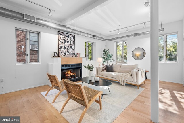 living room with a glass covered fireplace, rail lighting, hardwood / wood-style floors, and visible vents