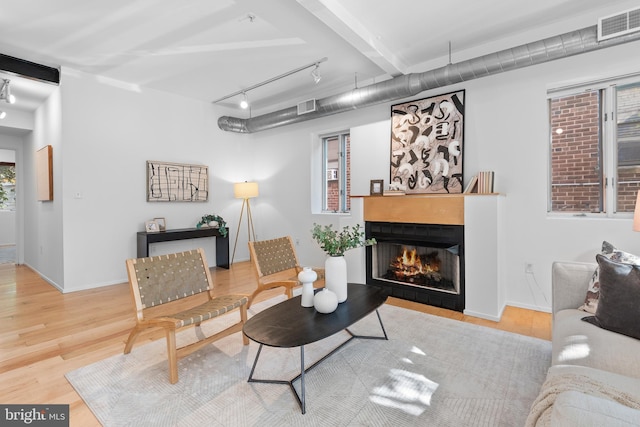 living area with a warm lit fireplace, rail lighting, visible vents, and wood finished floors
