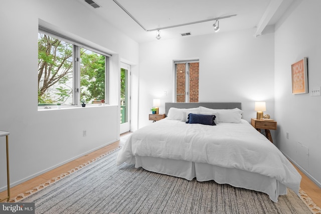 bedroom featuring access to outside, rail lighting, visible vents, and wood finished floors