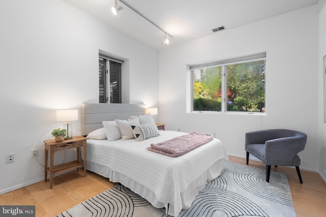 bedroom with light wood-style floors, baseboards, rail lighting, and visible vents