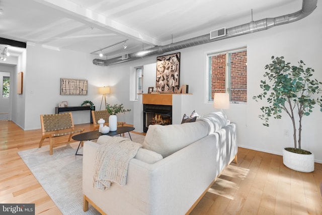 living room featuring a warm lit fireplace, visible vents, track lighting, and wood finished floors