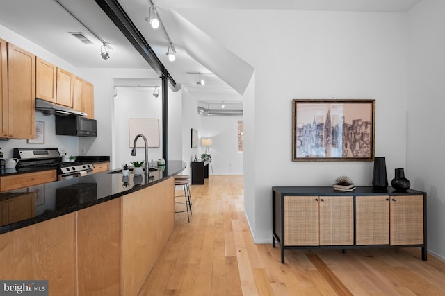 kitchen featuring a sink, stainless steel gas range oven, rail lighting, light wood-style flooring, and a kitchen bar