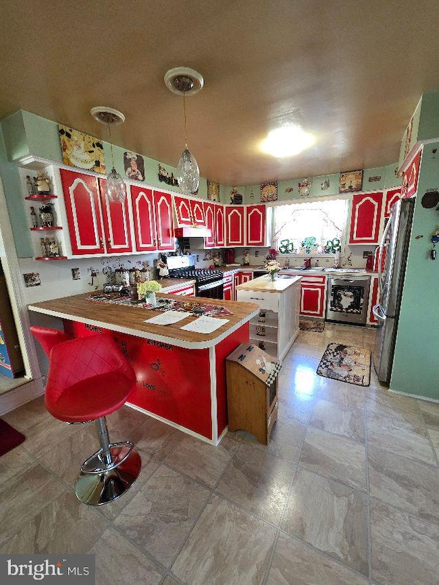 kitchen with a peninsula, freestanding refrigerator, light countertops, under cabinet range hood, and gas range