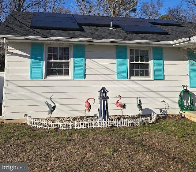 view of front facade with solar panels and roof with shingles