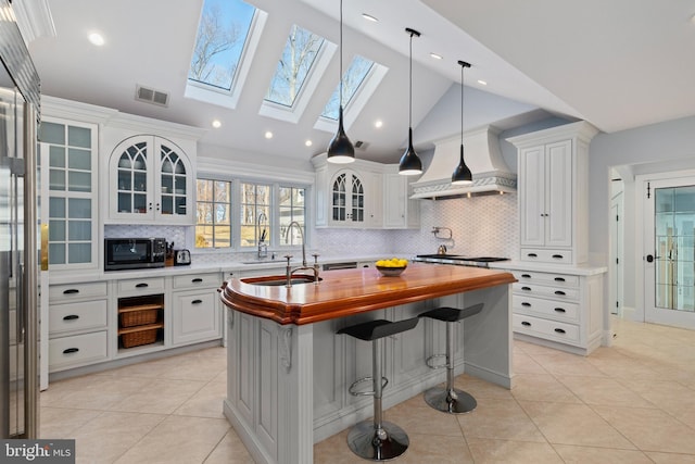 kitchen with white cabinetry, an island with sink, visible vents, and butcher block countertops