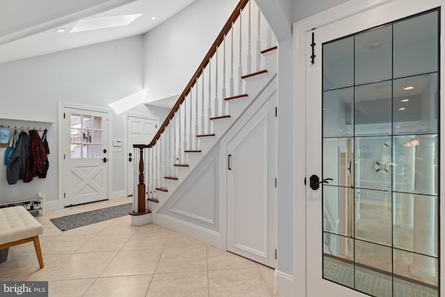 entrance foyer featuring light tile patterned flooring, a skylight, and stairs