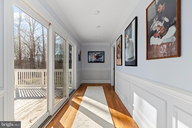 doorway to outside with a decorative wall, wainscoting, light wood-style floors, and ornamental molding