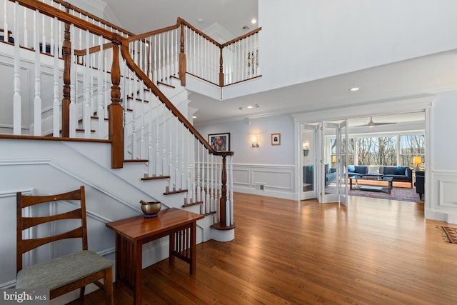 stairs with crown molding, a decorative wall, wood finished floors, and ceiling fan