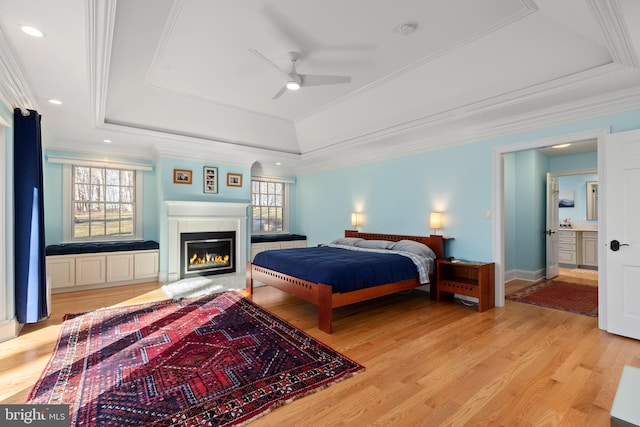 bedroom featuring a tray ceiling, recessed lighting, ornamental molding, light wood-style floors, and a glass covered fireplace