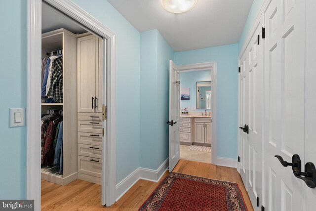 hall with light wood-style flooring, baseboards, and a sink