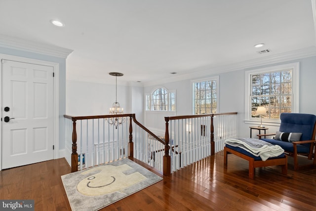 living area with visible vents, wood-type flooring, an inviting chandelier, and ornamental molding