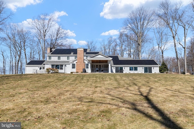 back of house with a porch, a yard, roof mounted solar panels, and a chimney