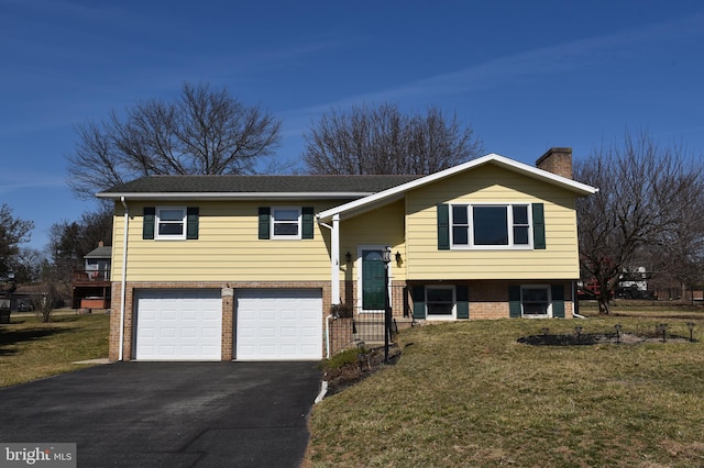 split foyer home featuring aphalt driveway, a front yard, brick siding, and a chimney