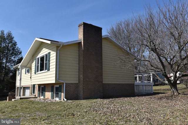 view of home's exterior featuring a yard, brick siding, a deck, and a chimney