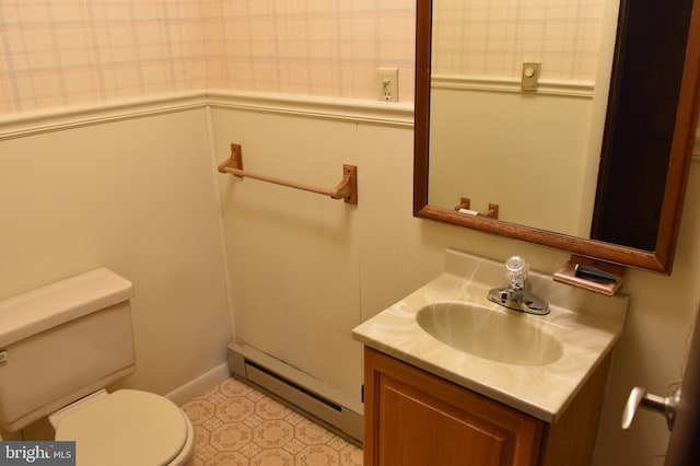 half bath with a wainscoted wall, vanity, toilet, and a baseboard heating unit