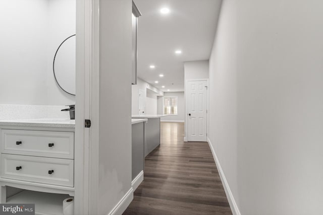 corridor with recessed lighting, baseboards, dark wood-type flooring, and a sink