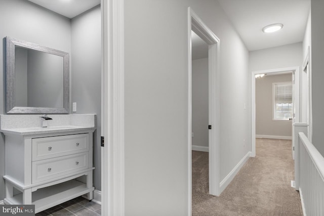 hall with a sink, baseboards, and carpet floors