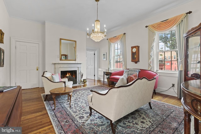 living room with a chandelier, ornamental molding, a warm lit fireplace, and dark wood-style flooring