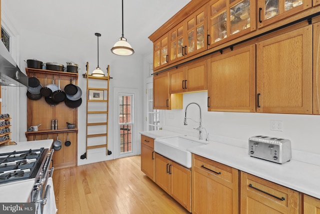 kitchen with gas stove, a sink, light countertops, decorative light fixtures, and light wood-type flooring