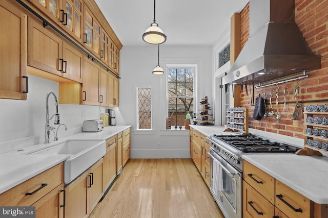 kitchen featuring light wood-style flooring, a sink, high end stainless steel range oven, wall chimney range hood, and hanging light fixtures