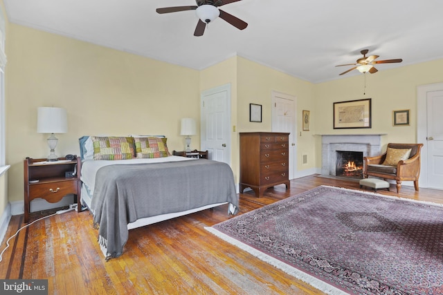 bedroom with a ceiling fan, wood finished floors, baseboards, and a lit fireplace