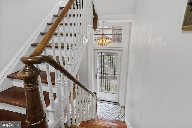 staircase with wood finished floors, baseboards, and a chandelier