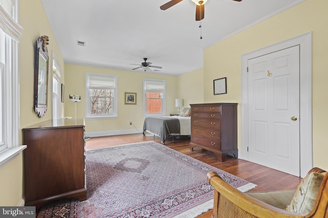 bedroom with ceiling fan, visible vents, baseboards, and wood finished floors