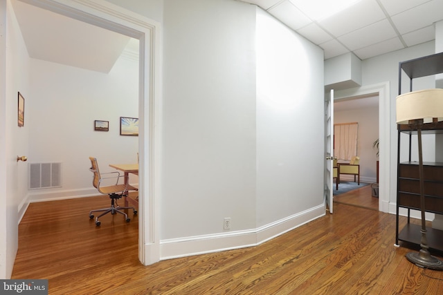 hall with wood finished floors, a paneled ceiling, visible vents, and baseboards