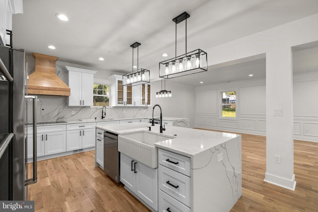 kitchen with custom exhaust hood, white cabinets, appliances with stainless steel finishes, and a sink