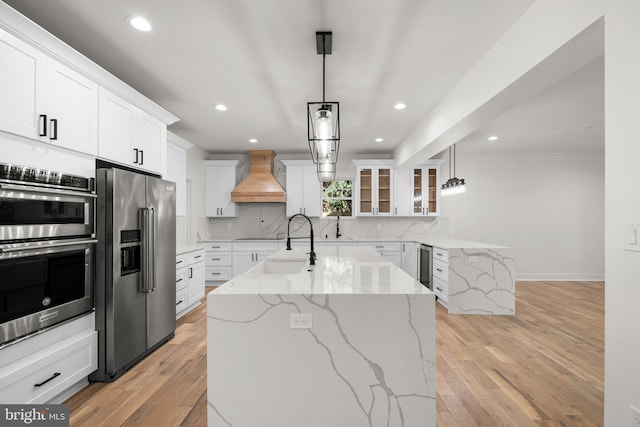 kitchen with custom exhaust hood, decorative backsplash, glass insert cabinets, appliances with stainless steel finishes, and white cabinetry