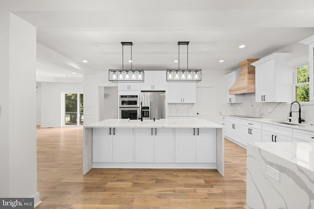 kitchen with a sink, backsplash, white cabinetry, stainless steel appliances, and custom exhaust hood